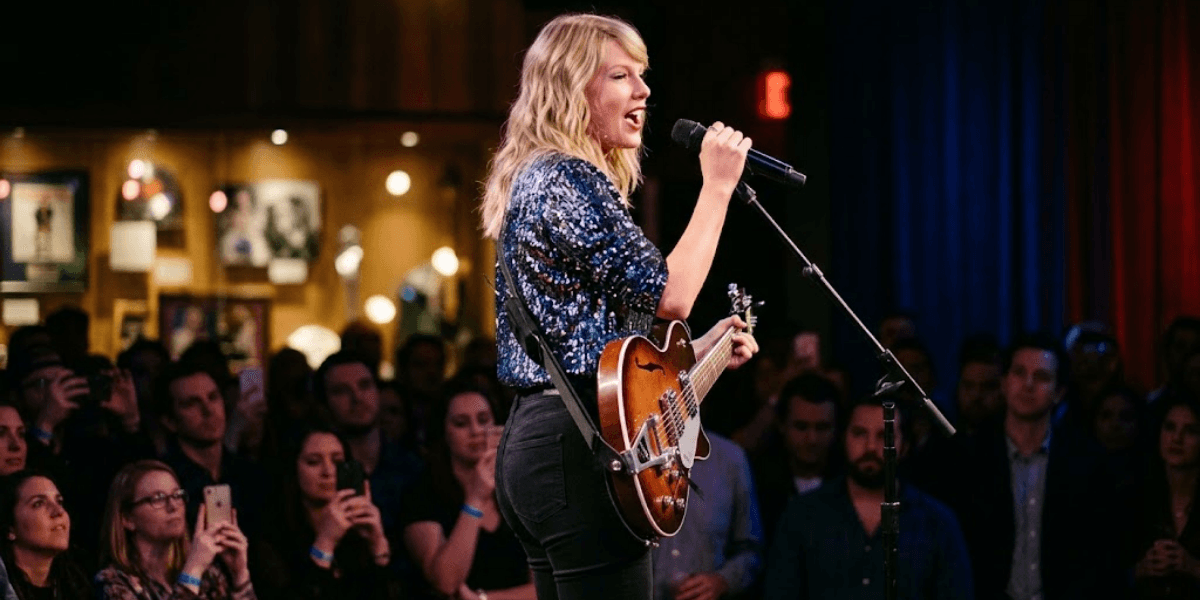 Woman performing on stage with a guitar, audience watching attentively in a venue