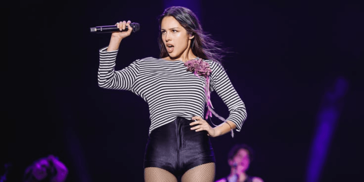 Singer performs on stage, holding a microphone, wearing a striped top and shorts