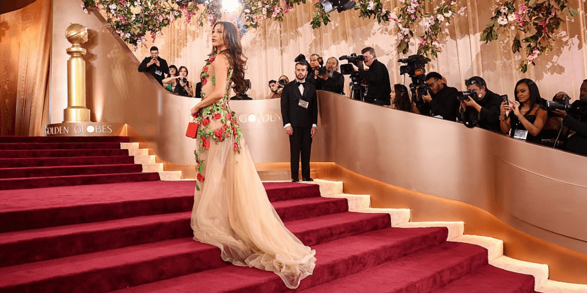 A glamorous figure in a floral gown walks down the Golden Globes red carpet.