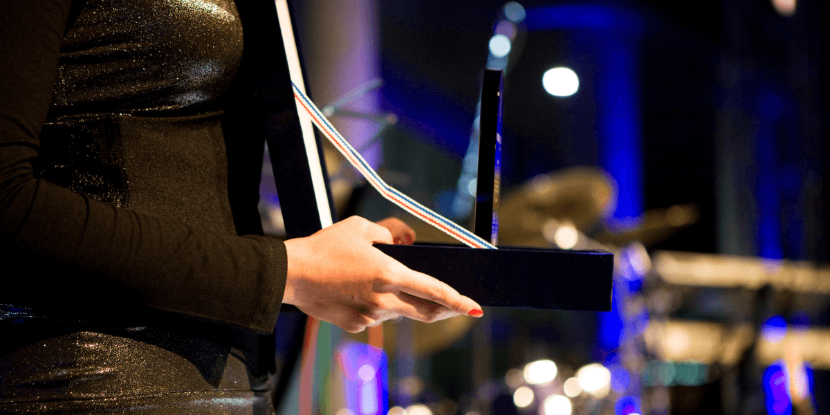 A person holds an award trophy onstage with instruments in the background