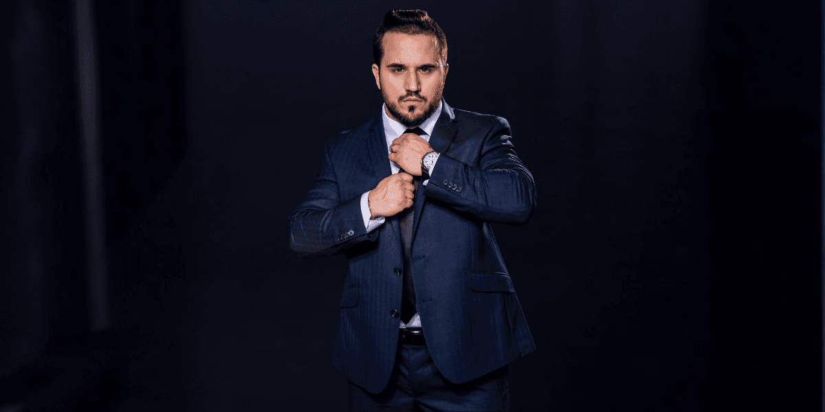 Man in a blue suit adjusting his tie against a dark background