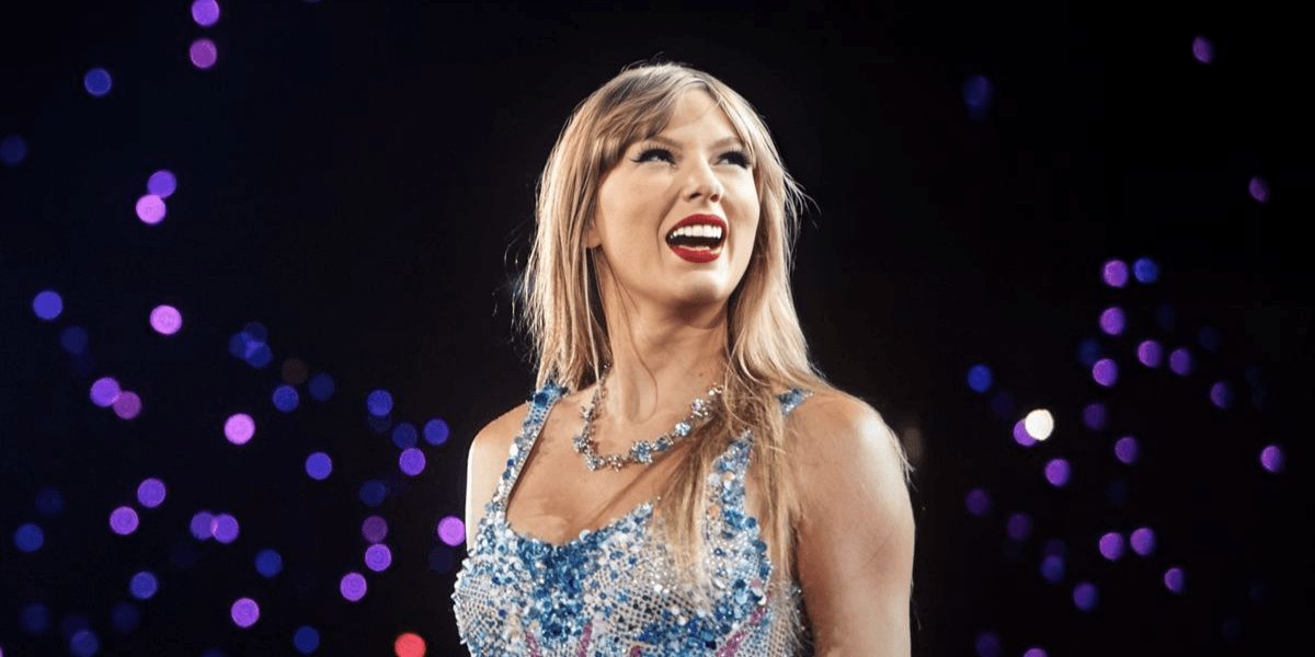 A performer in a sparkling outfit smiles brightly on stage with vibrant lights behind.