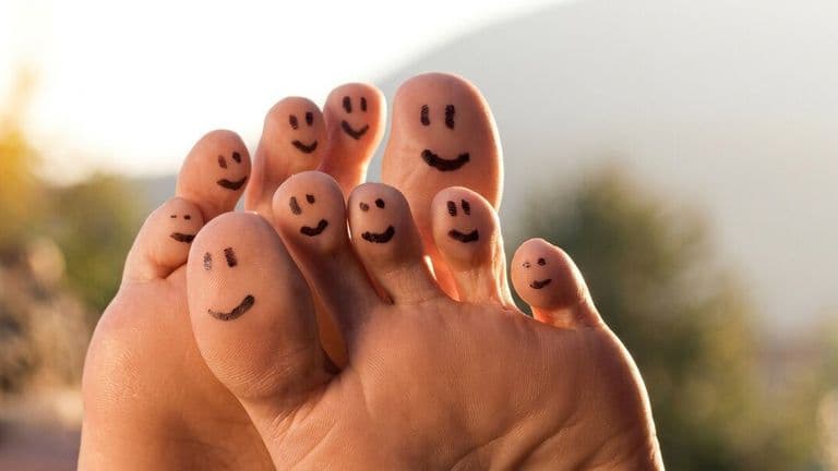 Smiling faces drawn on toes, illustrating comfort, confidence, and playful foot care outdoors.