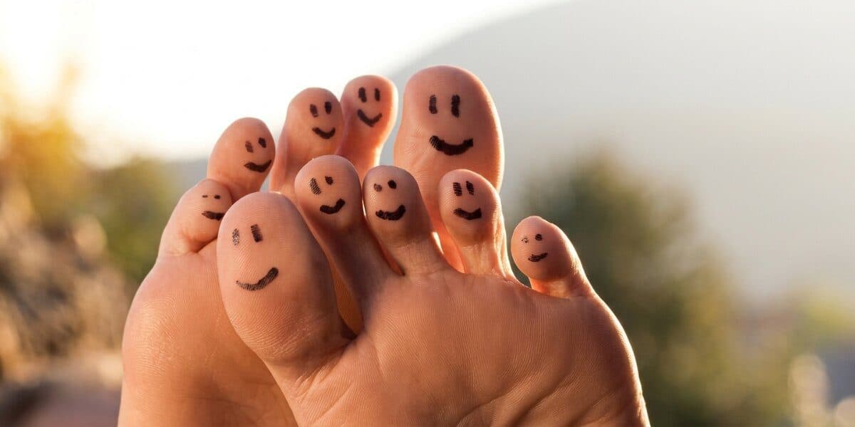 Smiling faces drawn on toes, illustrating comfort, confidence, and playful foot care outdoors.