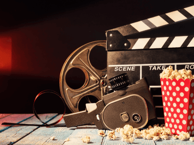 Vintage film camera, reel, clapperboard, and popcorn arranged on a table under cinematic lighting.