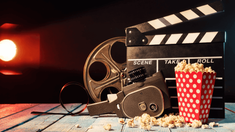 Vintage film camera, reel, clapperboard, and popcorn arranged on a table under cinematic lighting.