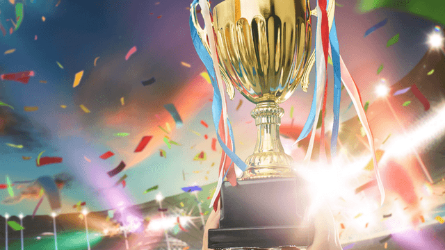 Gold championship trophy with colorful ribbons and confetti in a brightly lit stadium.