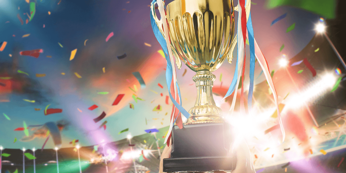 Gold championship trophy with colorful ribbons and confetti in a brightly lit stadium.