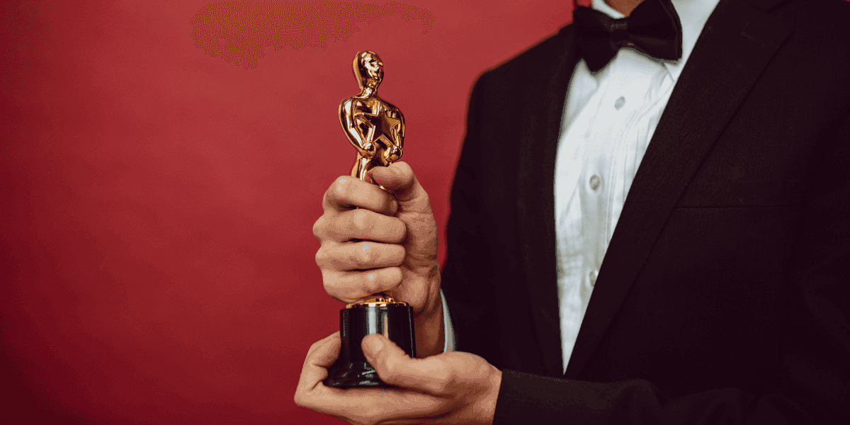 Person in a tuxedo holding a gold award statuette against a red background.