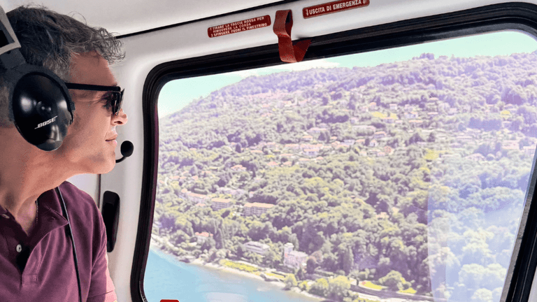 Man looking out the window of a helicopter, observing the beautiful landscape and hills during a scenic flight.