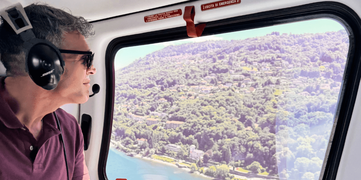 Man looking out the window of a helicopter, observing the beautiful landscape and hills during a scenic flight.
