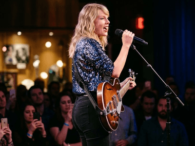 Woman performing on stage with a guitar, audience watching attentively in a venue