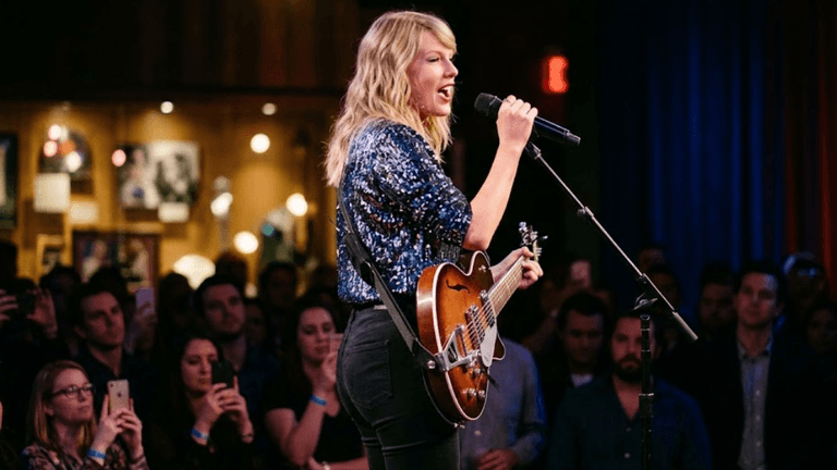 Woman performing on stage with a guitar, audience watching attentively in a venue
