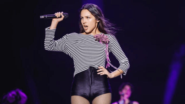 Singer performs on stage, holding a microphone, wearing a striped top and shorts