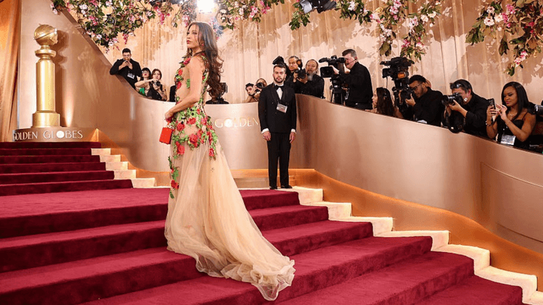 A glamorous figure in a floral gown walks down the Golden Globes red carpet.