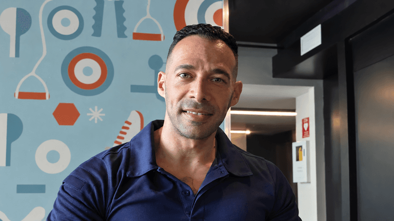 Man in a navy polo shirt smiling against a colorful patterned wall backdrop