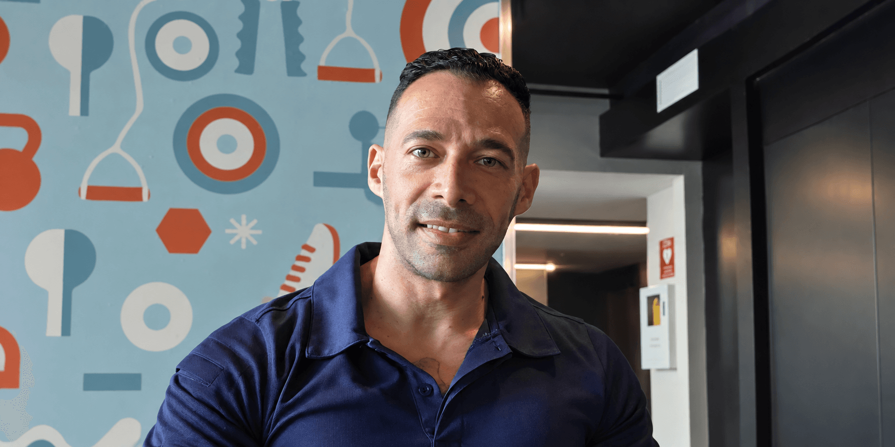 Man in a navy polo shirt smiling against a colorful patterned wall backdrop