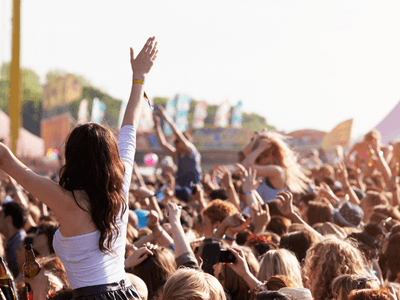 Crowd at a music festival with a woman on someone's shoulders celebrating joyfully