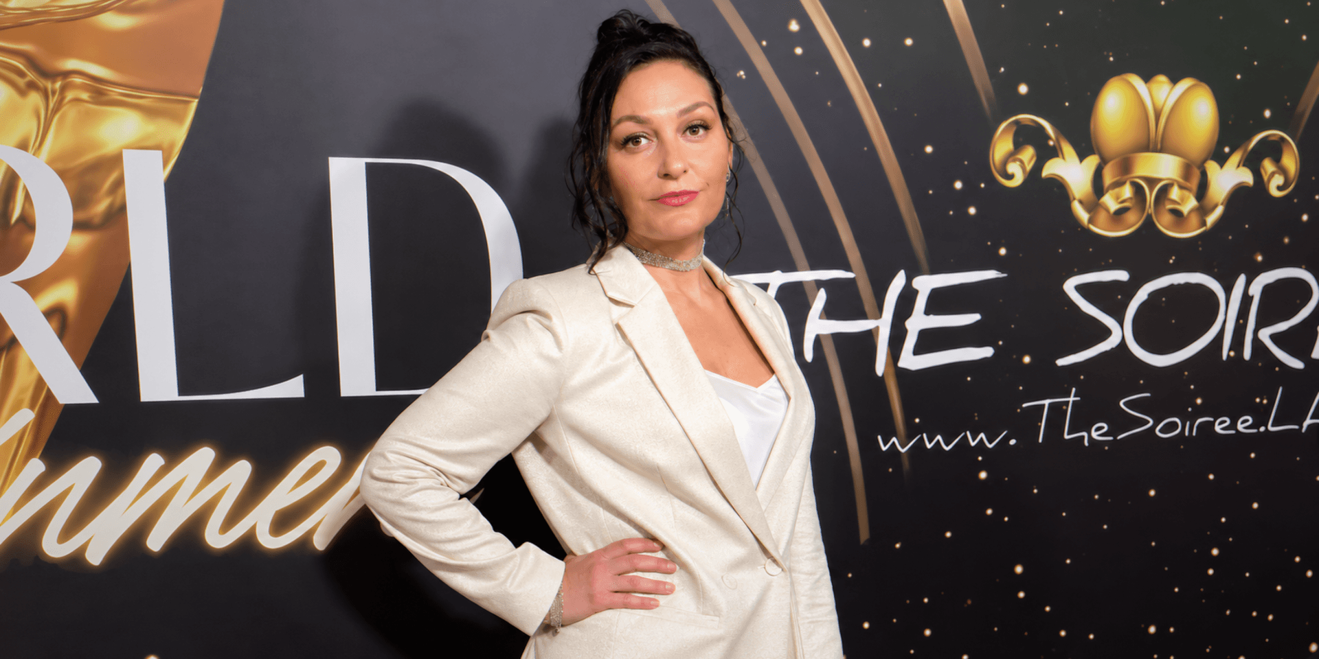 Woman in a blazer poses confidently at a glamorous event backdrop