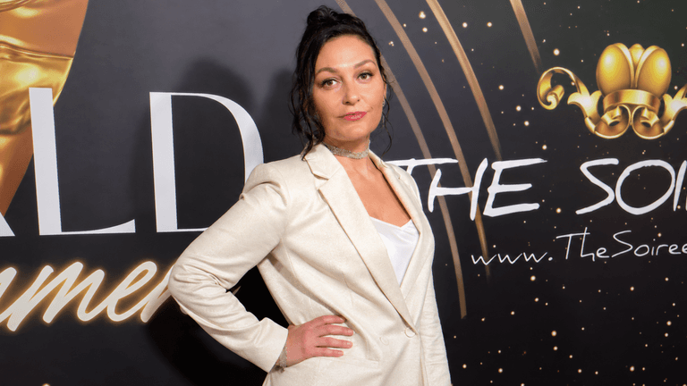 Woman in a blazer poses confidently at a glamorous event backdrop