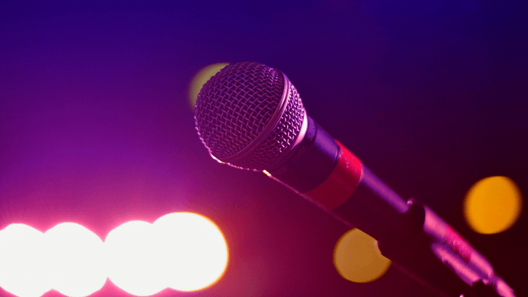 Close-up of a microphone against a colorful, blurred background of stage lights