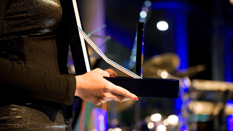 A person holds an award trophy onstage with instruments in the background