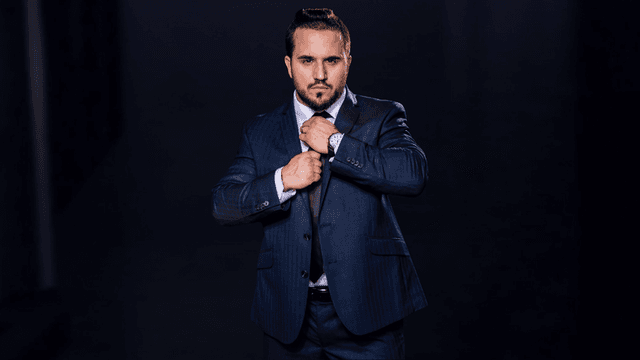 Man in a blue suit adjusting his tie against a dark background