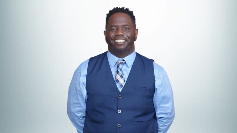 Rashad Woods, a black man in a blue shirt and vest, leads The T.R.O.N. Podcast, inspiring growth through global conversations.