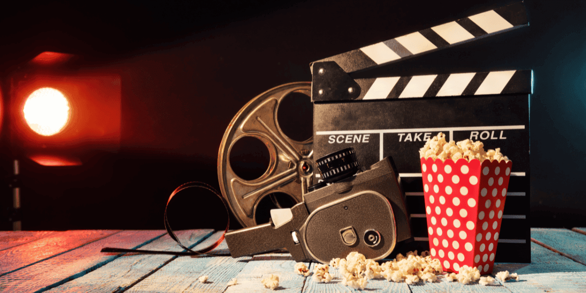 Vintage film camera, reel, clapperboard, and popcorn arranged on a table under cinematic lighting.