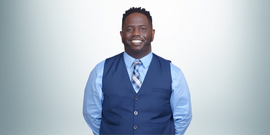 Rashad Woods, a black man in a blue shirt and vest, leads The T.R.O.N. Podcast, inspiring growth through global conversations.