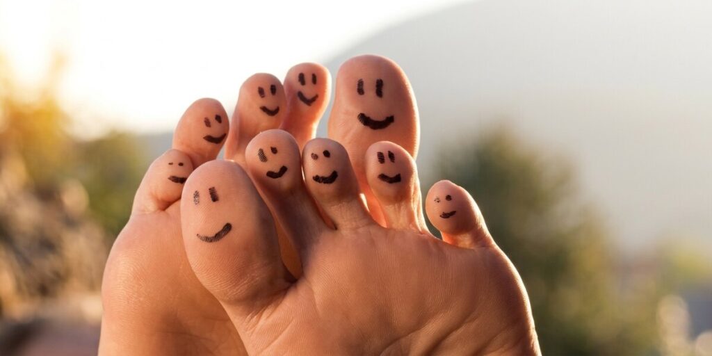 Smiling faces drawn on toes, illustrating comfort, confidence, and playful foot care outdoors.