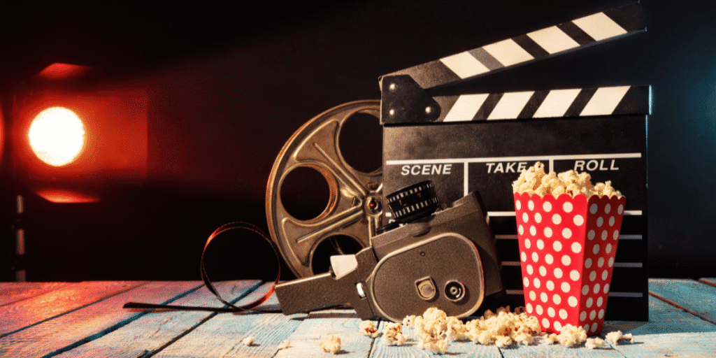 Vintage film camera, reel, clapperboard, and popcorn arranged on a table under cinematic lighting.